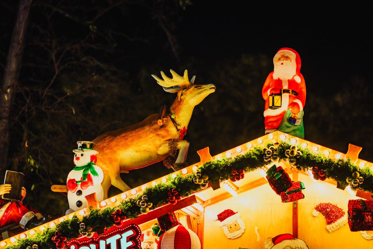 Illuminated Santa and reindeer figures with garland and warm bulbs along the roof edge of a festive market stall at night
